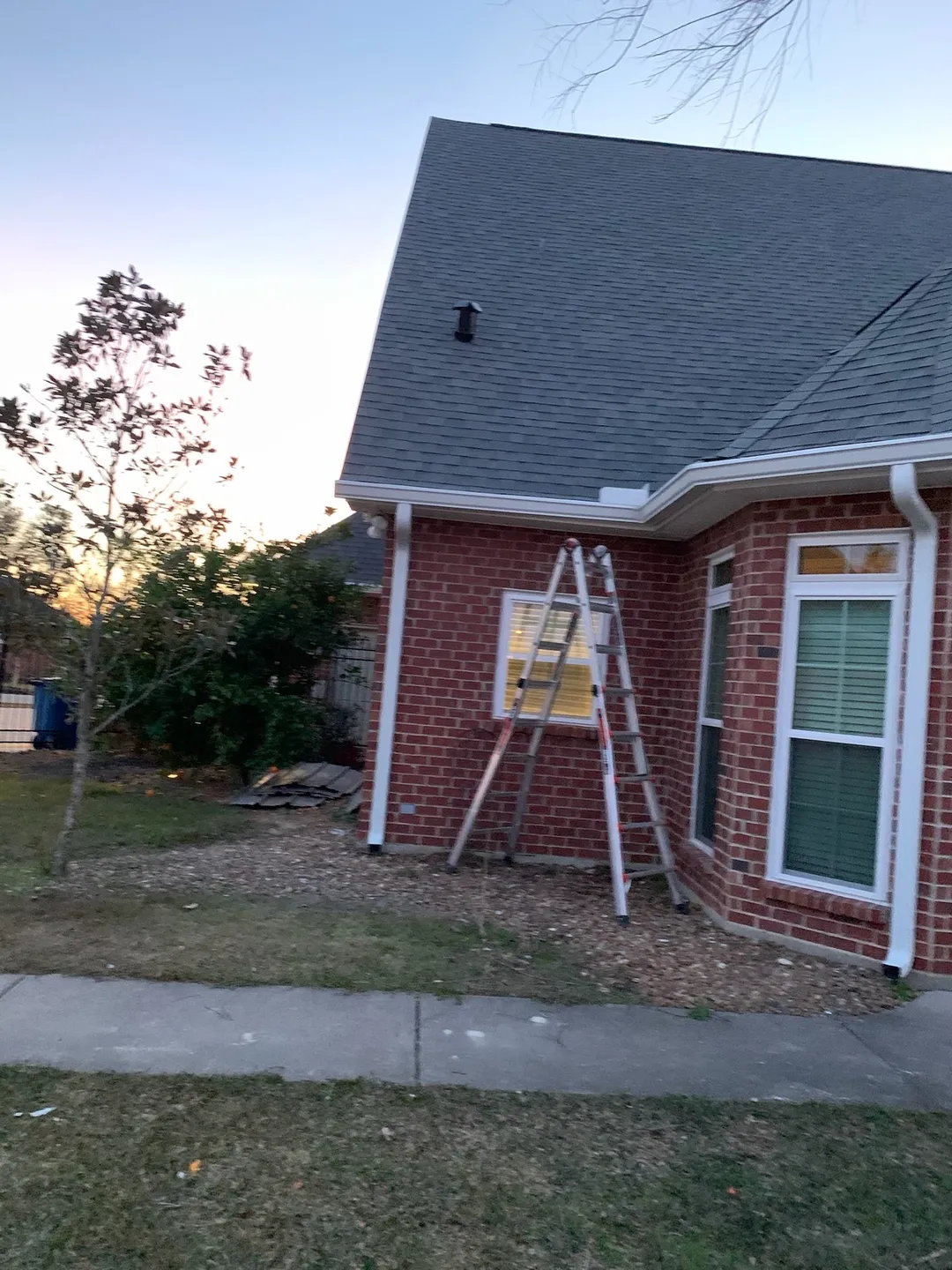 ladder in front of brick home with white gutters at sunset