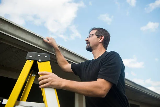 man on ladder inspecting gutters