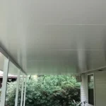 Underside of a white insulated aluminum patio cover on a Louisiana home, showing the flat finished ceiling and slim support posts.