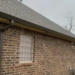 Long gutter run and downspout on a brick home, viewed from the ground to judge gutter age
