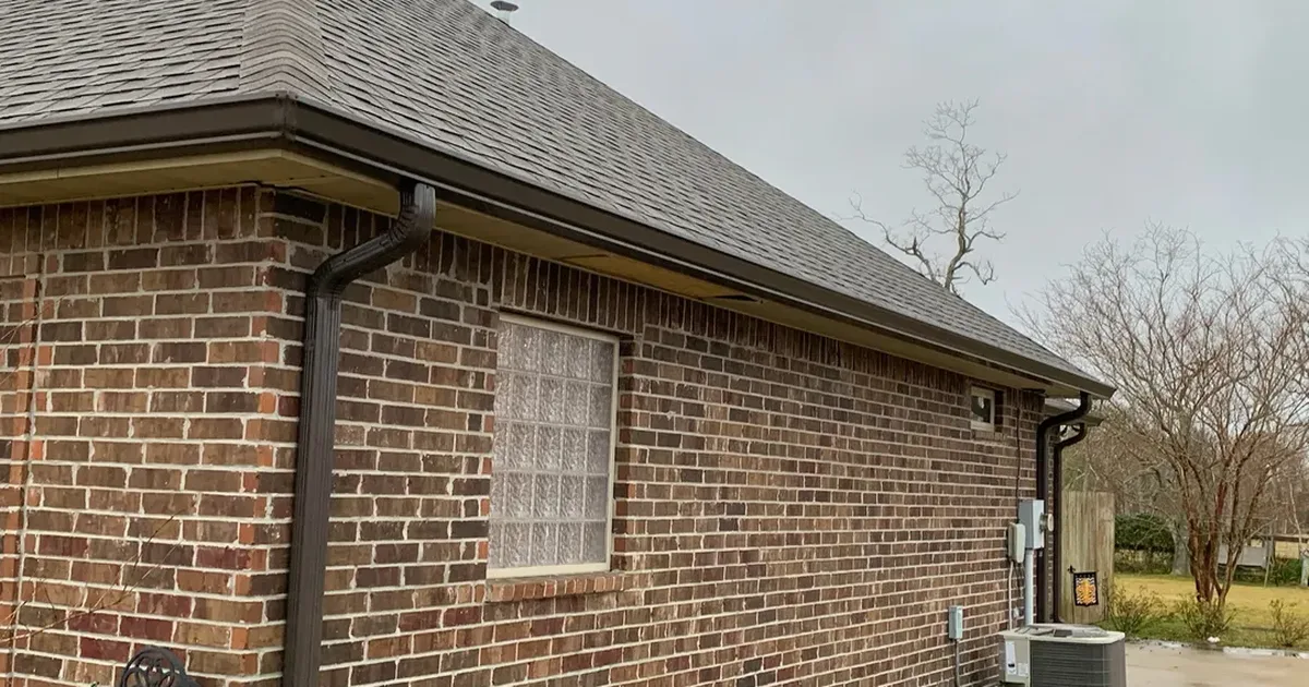 Long gutter run and downspout on a brick home, viewed from the ground to judge gutter age