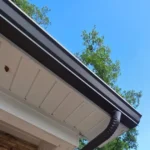 Brown seamless gutter and downspout on a brick home with live oak branches above the roofline