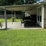 Attached aluminum patio cover with gutter and downspout over a stamped concrete patio on a brick home