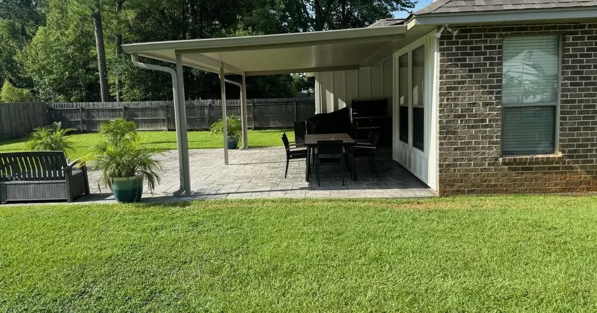 Attached aluminum patio cover with gutter and downspout over a stamped concrete patio on a brick home