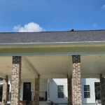 Long white seamless gutter running the full front edge of a wide brick-column carport, with a downspout at each end